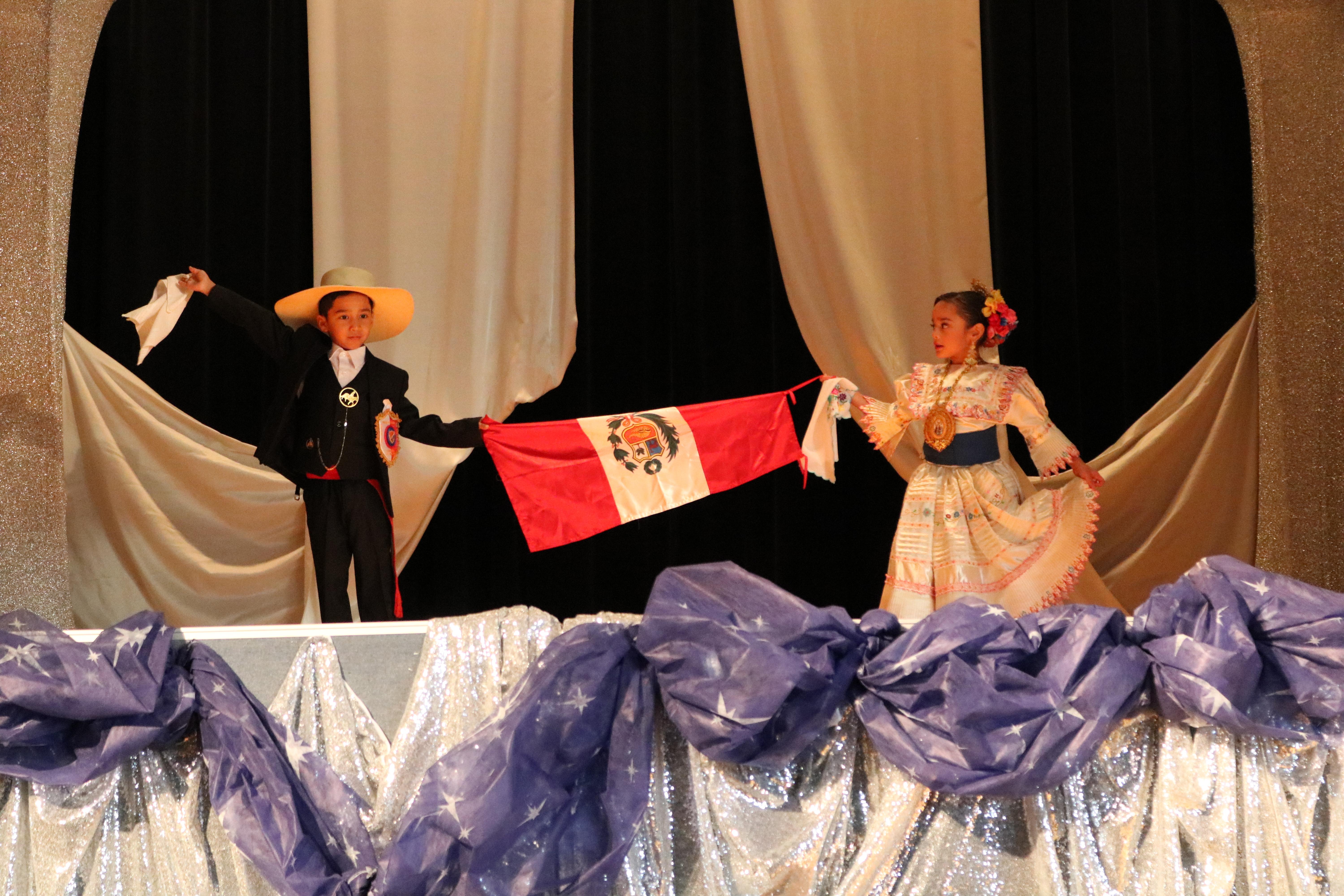 two children dressed in the Peruvian cultural dress holding the Peruvian flag